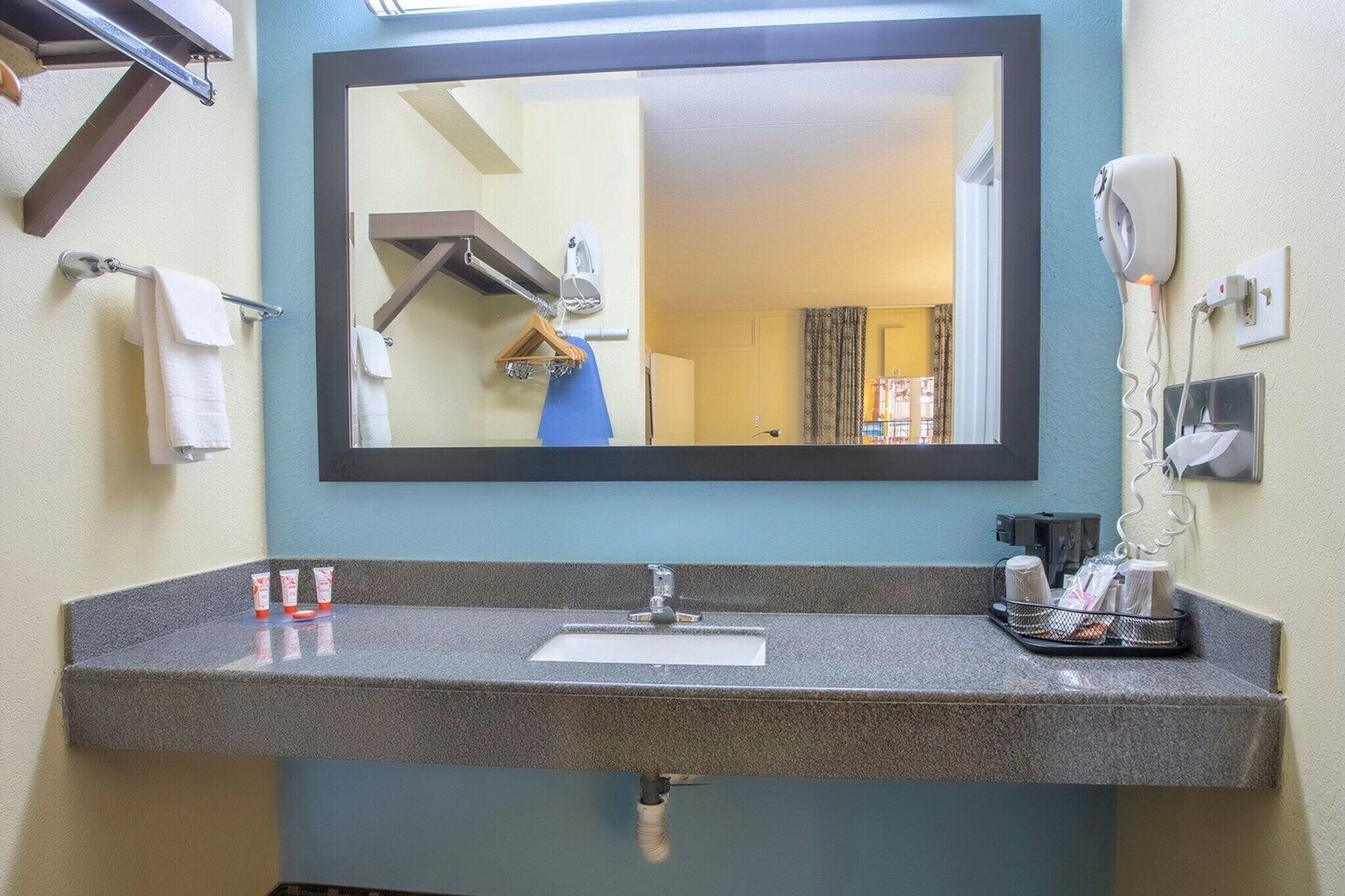 A bathroom with a sink, mirror, towel rack, hairdryer, and toiletries.