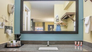 A bathroom with a large mirror, a sink, a hairdryer, and toiletries on the counter.