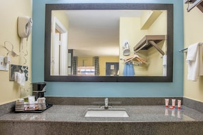 Un baño con un espejo grande, un lavabo, un secador de pelo y artículos de aseo.