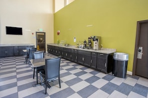 Un suelo a cuadros, asientos tipo bar, una máquina de café y un cubo de basura en una habitación con una pared de acento verde.