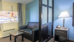 A hotel room with a black leather sofa, a small table, a lamp, a telephone, and a window with a view of a building.