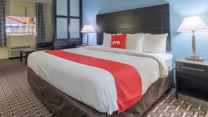 A hotel room with a large bed, a nightstand, a lamp, a window with curtains, and a view of a building outside.