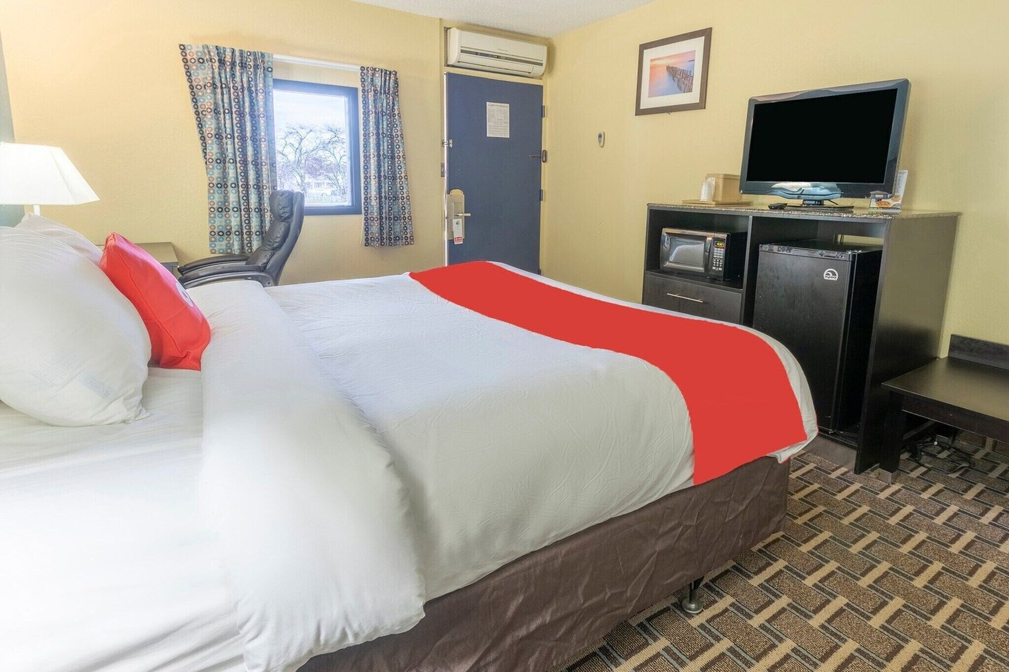Une chambre d’hôtel avec un lit, un bureau équipé d’un ordinateur, une télévision et une fenêtre avec des rideaux.