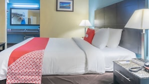 Habitación de hotel con cama, mesita de noche con lámpara, teléfono e imagen en la pared.