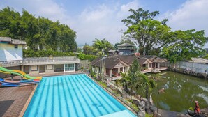 A swimming pool with a slide, surrounded by houses and a pond. - Hotel Danau Tjokro 3 By ARBA (Cisarua)