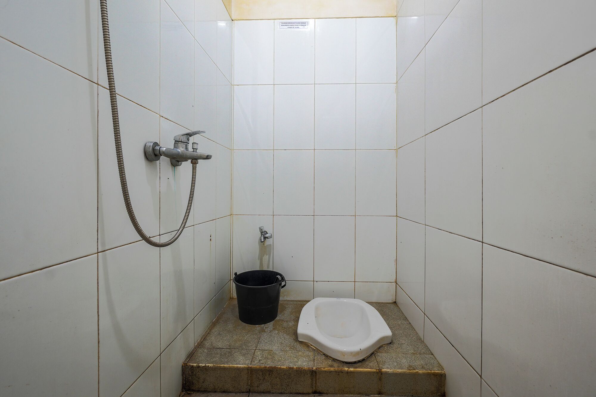 Un baño pequeño con azulejos, ducha, inodoro y un balde.
