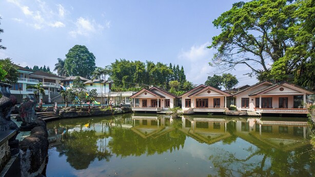 A tranquil lakeside setting with traditional-style buildings, a clear sky, and a calm water surface reflecting the structures. - Hotel Danau Tjokro 3 By ARBA (Cisarua)