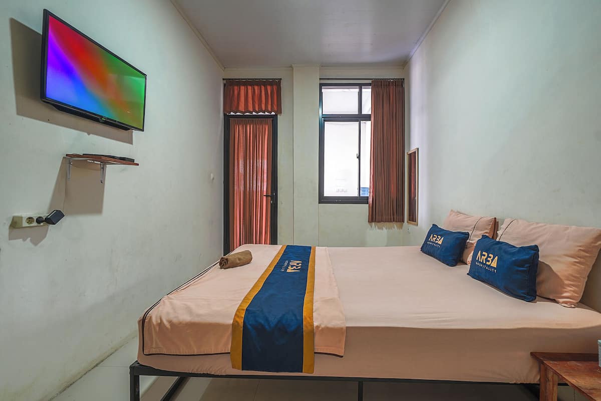 Habitación de hotel con cama, televisión montada en la pared y ventana con cortinas.