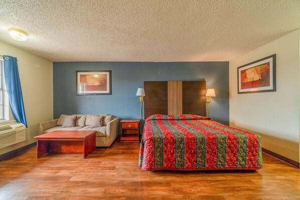A bedroom with a bed, a sofa, a coffee table, two lamps, and framed pictures on the walls.
