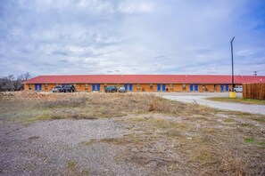 Ein Motel mit rotem Dach und blauen Türen, einem Parkplatz mit Kiesbelag und einem Holzzaun.