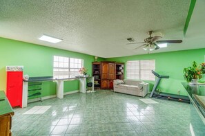 A room with green walls, a red cabinet, a treadmill, a ceiling fan, and a window.