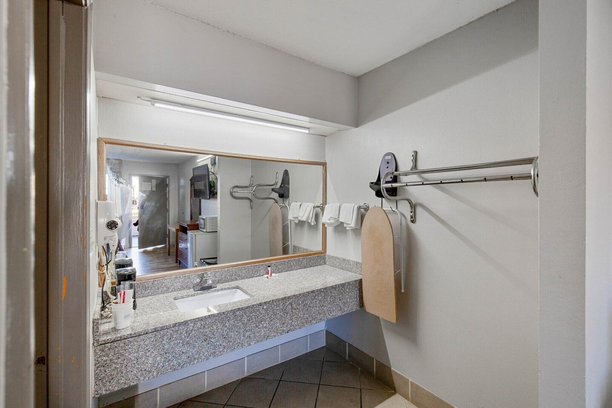 A bathroom with a granite countertop, a sink, a mirror, a towel rack, and a shower area.
