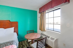 Una habitación de hotel con cama, una mesa redonda, una silla, ventana con cortinas y aire acondicionado instalado en la pared.