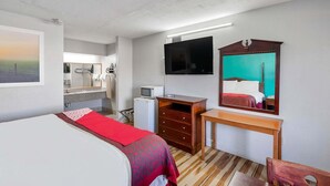 A hotel room with a bed, a desk, a TV, a mirror, a small fridge, and a bathroom visible in the background. - King Bed Smoking with Jetted Tub (Columbia)