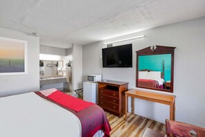 A hotel room with a bed, a desk, a TV, a mirror, a small fridge, and a bathroom visible in the background.