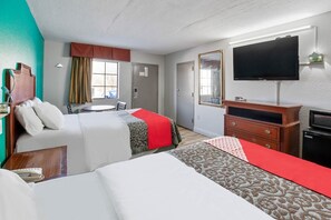 A hotel room with two beds, a television, a dresser, and a window with curtains.