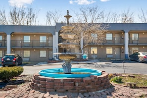 A multi-story motel with a central fountain, outdoor parking, and a brick facade. - 2 Full Beds | Non Smoking (Columbia)