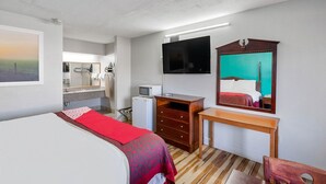 A hotel room with a bed, a desk, a mirror, a television, and a small kitchenette.