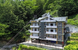 A multi-story building with balconies, surrounded by dense forest. - Aranya Retreat Himachal (Mananli)
