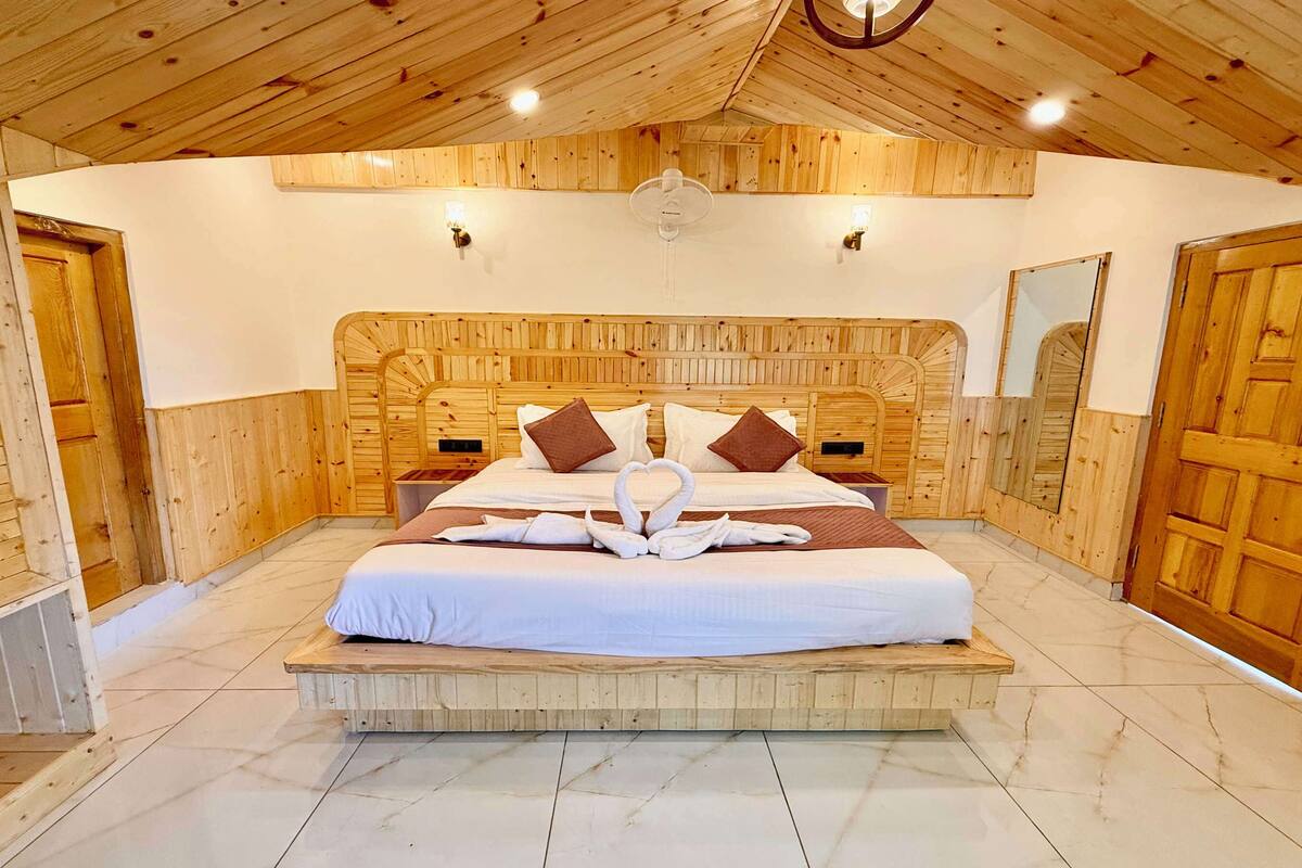 A wooden-paneled bedroom with a large bed, a ceiling fan, and two wall-mounted lights.