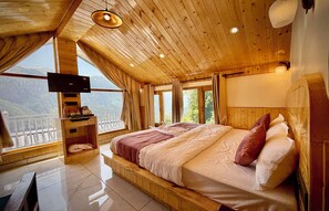 Ein Zimmer mit Holzboden, einem Bett, einem Fernseher und Blick auf die Berge.