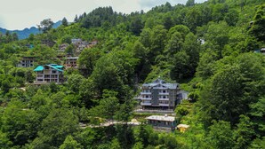 A hillside village with multiple buildings surrounded by dense greenery. - Aranya Retreat Himachal (Manali)