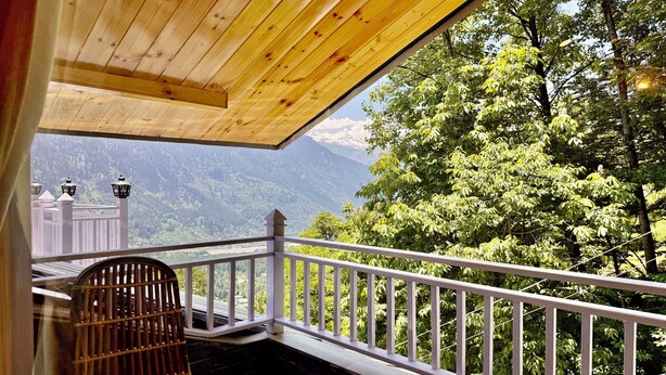 A wooden balcony with a railing, a chair, and a view of a mountainous landscape. - Aranya Retreat Himachal (Manali)