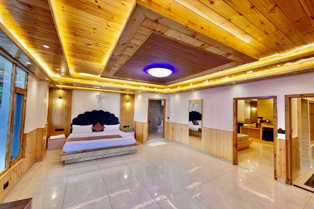 A modern hotel room with a wooden ceiling, a large bed, a bathroom with a mirror, and a view of the outside.