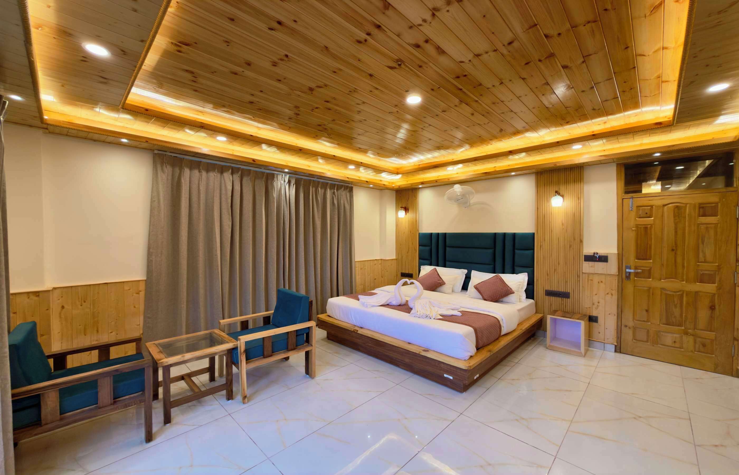 A hotel room with a wooden ceiling, a bed with pillows, a small table, and a chair.