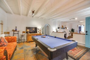 Una mesa de billar en una sala con sofá, televisión y zona de cocina.