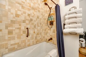 A bathroom with a tiled shower wall, a bathtub, a towel rack with folded towels, and a showerhead.