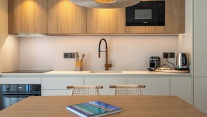 A modern kitchen with wooden cabinets, a stainless steel microwave, a coffee machine, and a book on the table. - Il Borgo Marina Homesuites Poltu Quatu (Arzachena)