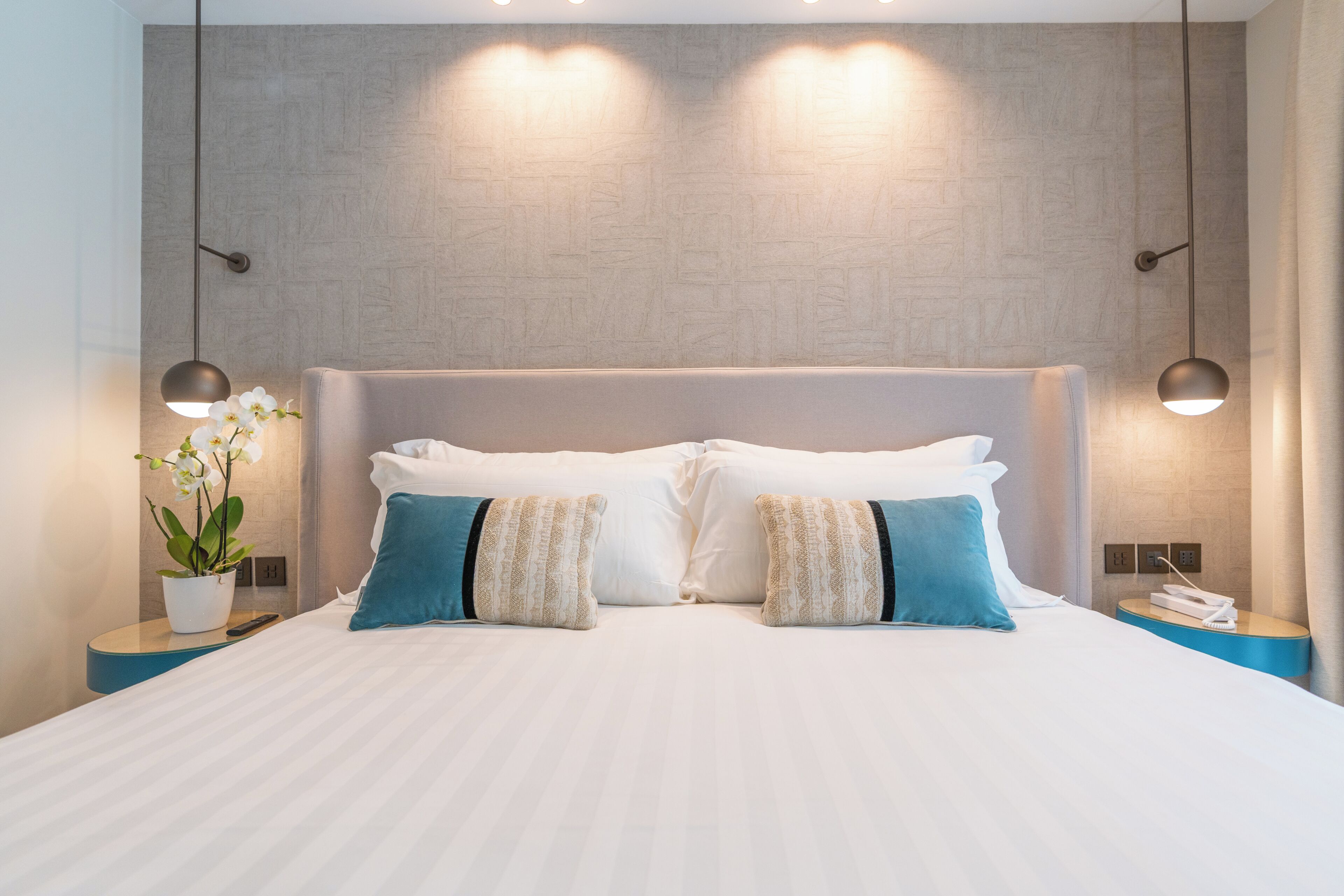 A neatly made bed with pillows, a bedside plant, and a nightstand with a phone.