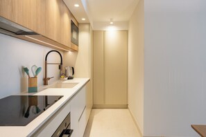 A modern kitchen with a black stove, wooden cabinets, a sink, and a coffee maker. - Il Borgo Marina Homesuites Poltu Quatu (Arzachena)
