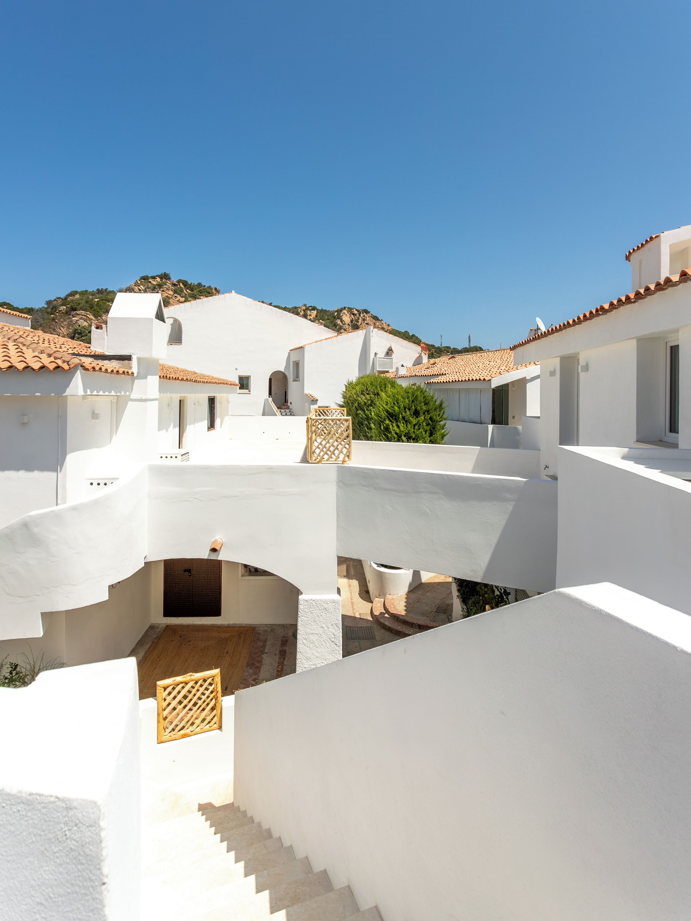 A white building with a tiled roof, a staircase, and a small garden area.