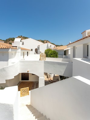 A white building with a tiled roof, a staircase, and a small garden area. - Il Borgo Marina Homesuites Poltu Quatu (Arzachena)