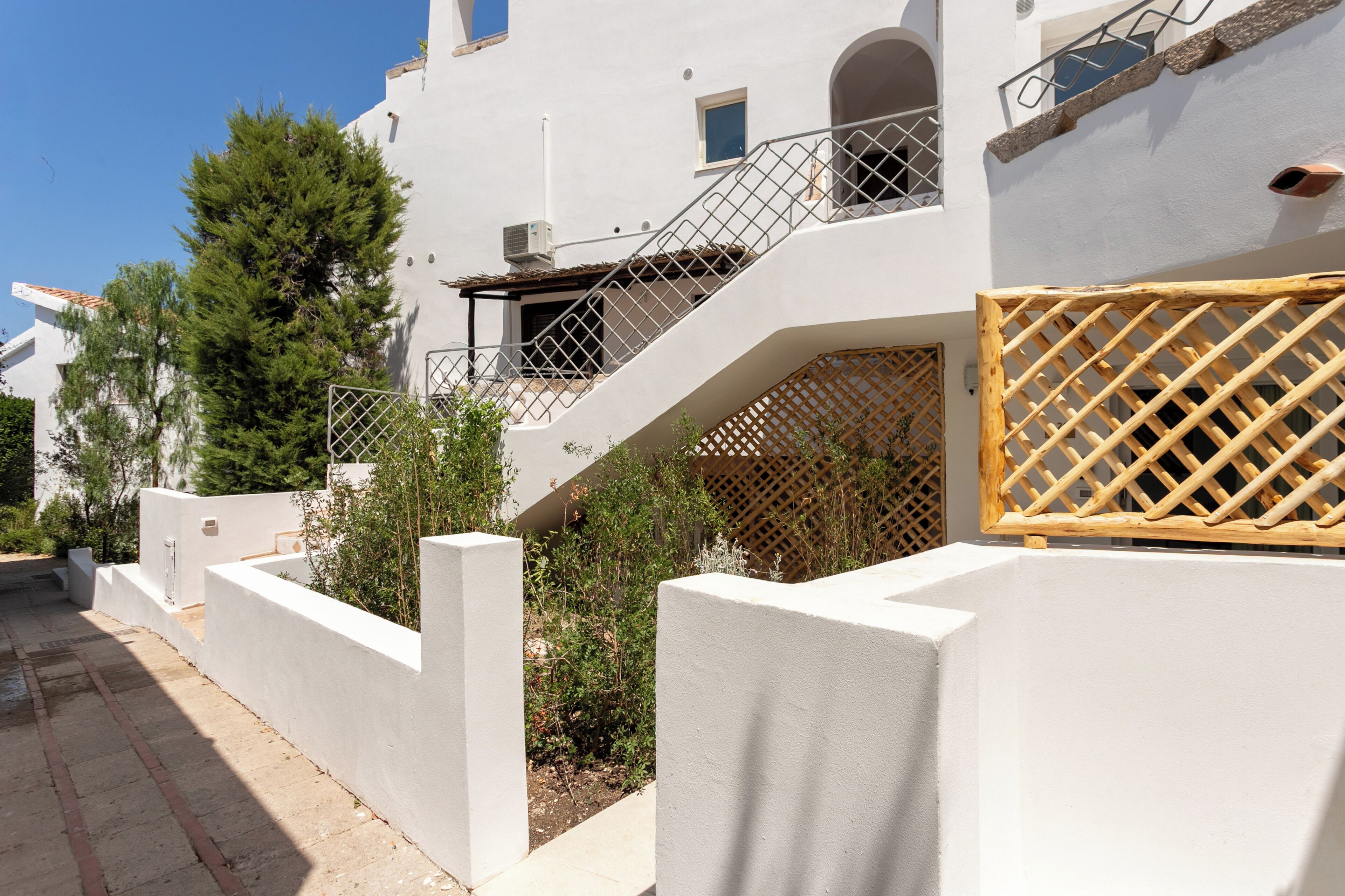 Un bâtiment blanc avec un escalier, une clôture en bois et de la verdure.