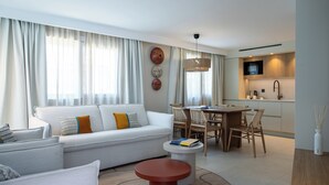 A modern living room with a sofa, dining table, and chairs, a kitchen area with a microwave, and a large window with curtains. - Il Borgo Marina Homesuites Poltu Quatu (Arzachena)