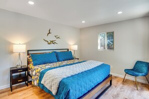 Ein Schlafzimmer mit einem Bett, zwei Nachttischen mit Lampen, einem Sessel, einem Fenster mit Jalousien und einer Wanddekoration.