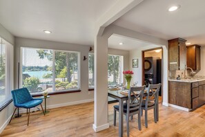 A dining area with a table set for four, a blue chair, and a vase of red flowers.