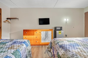 Une chambre d’hôtel avec deux lits, une commode en bois, un téléviseur à écran plat, un réfrigérateur et une lampe fixée au mur.