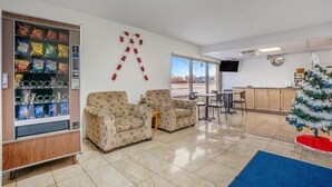 A living area with a vending machine, two patterned armchairs, a small table, a Christmas tree, and a kitchen area in the background. - 2 Queen Beds|Non-Smoking (Devils Lake, ND)