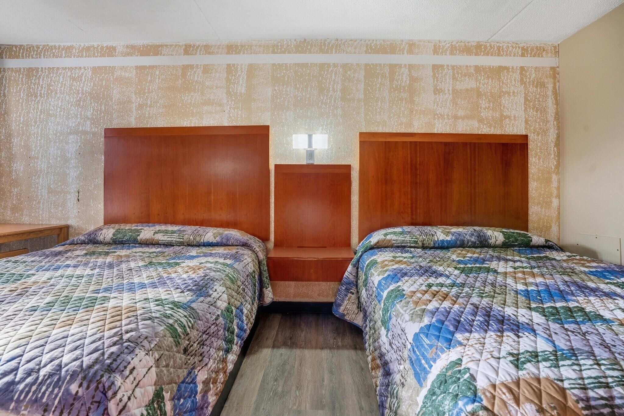 Hotellihuone, jossa on kaksi sänkyä, yöpöytä ja pieni pöytä, jossa on lamppu.