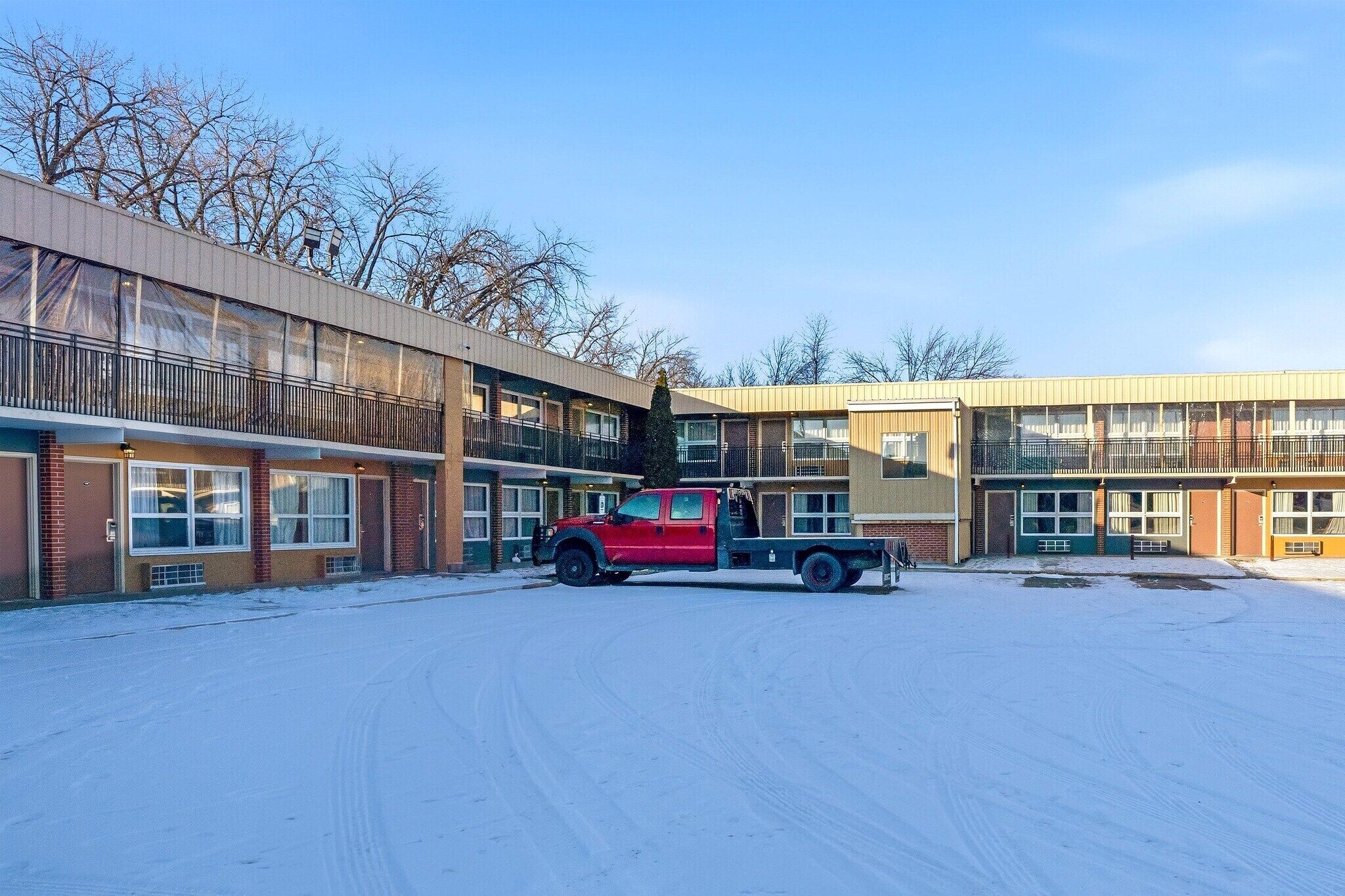 A multi-story motel with a red truck parked in front, snow on the ground, and a clear sky.