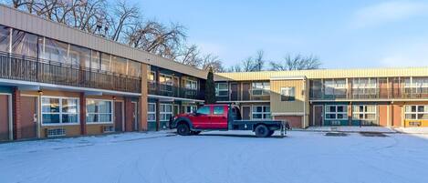 A multi-story motel with a red truck parked in front, snow on the ground, and a clear sky.