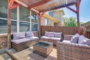 Eine überdachte Terrasse mit Korbmöbeln, einem Glastisch und einem Holzzaun.