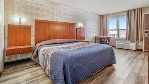 A hotel room with a large bed, wooden headboard, bedside tables, a desk, and a window with curtains. - King Bed|Non-Smoking (Devils Lake, ND)