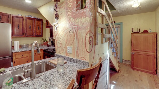 A kitchen with granite countertops, wooden cabinets, a stainless steel sink, and a wooden chair. - Home Near Eleven Point River & Nat'l Forest! (Alton)