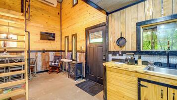 Un intérieur en bois comprenant un coin cuisine, une cheminée et une porte donnant sur l’extérieur.