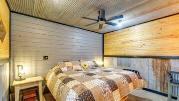 Quarto com cama, escrivaninha com luminária, cadeira e ventilador de teto.